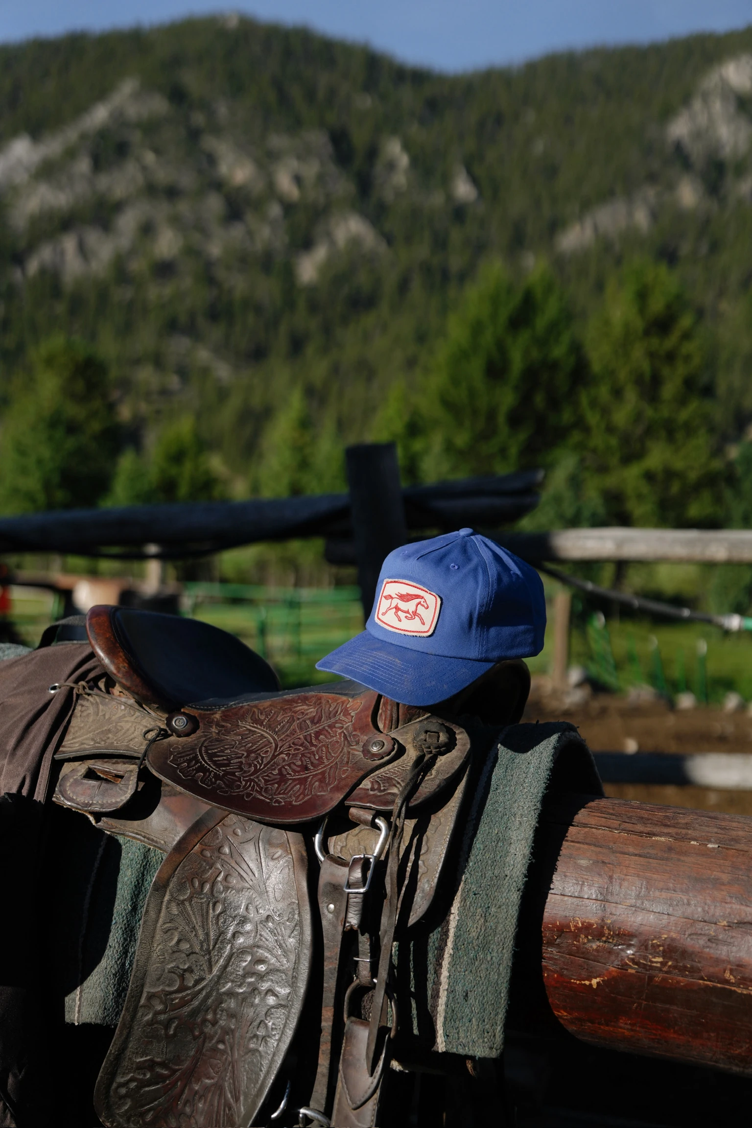 A blue Rustero cap resting on a leather saddle against a mountain landscape