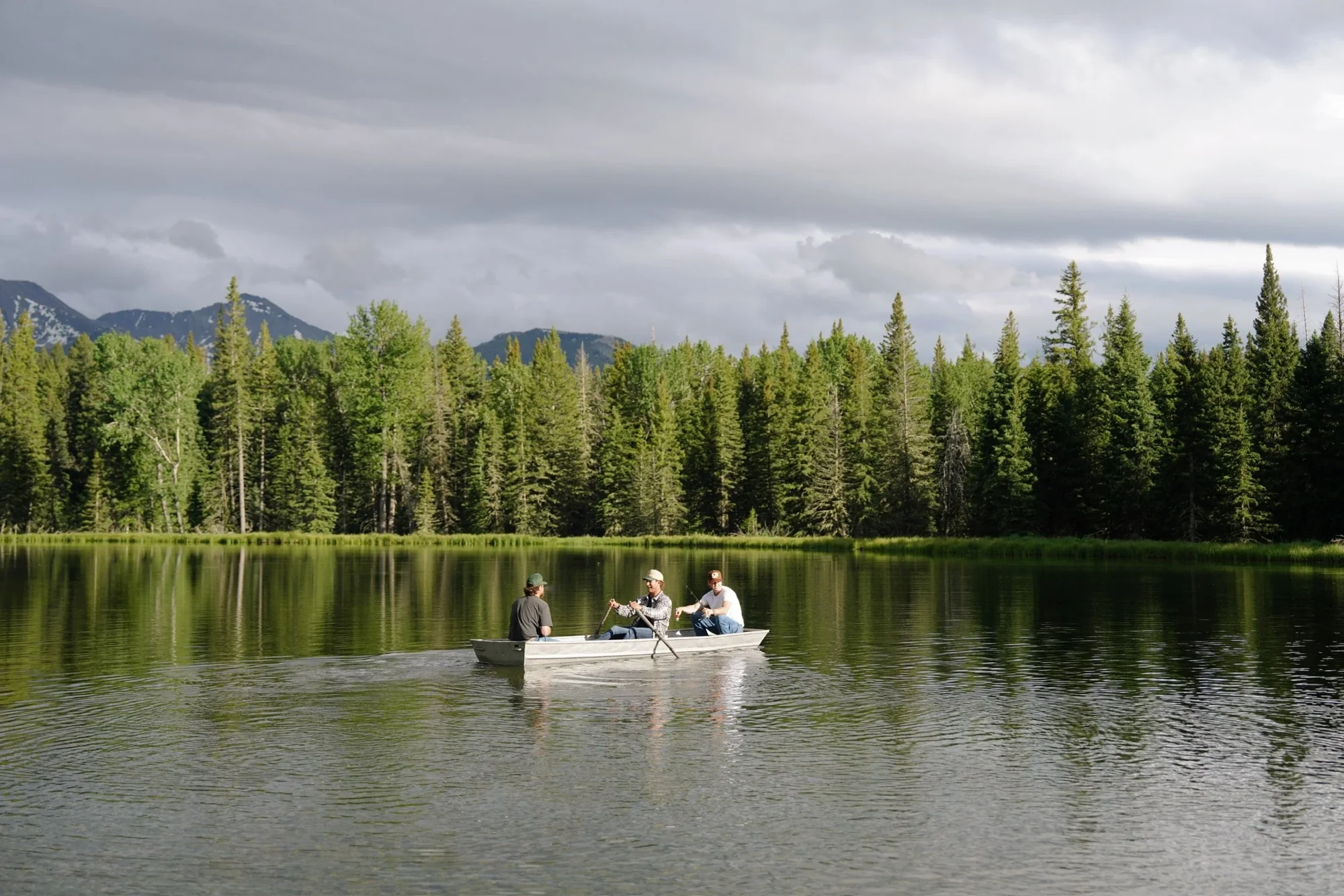 Three people in a canoe on a forest-lined lake, photographed for Elmat’s