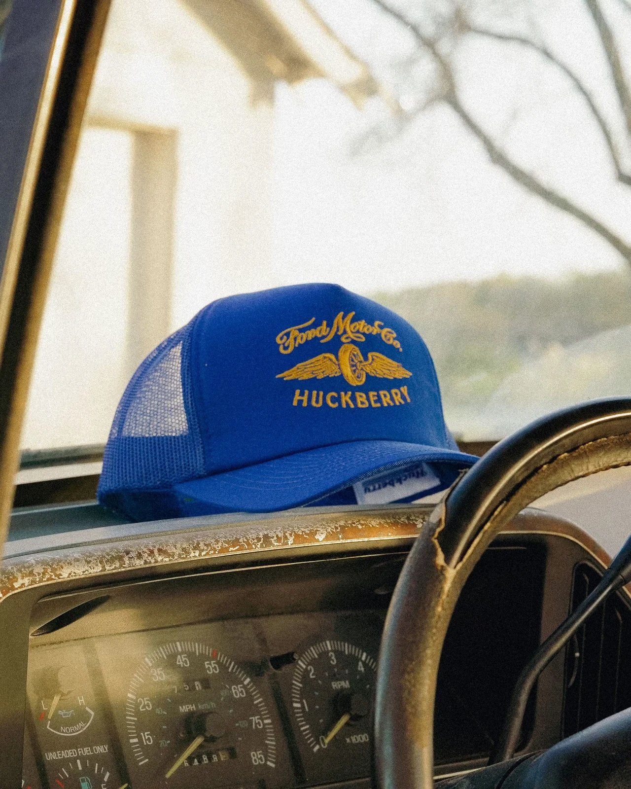 Blue Ford × Huckberry trucker hat resting on a vintage truck dashboard