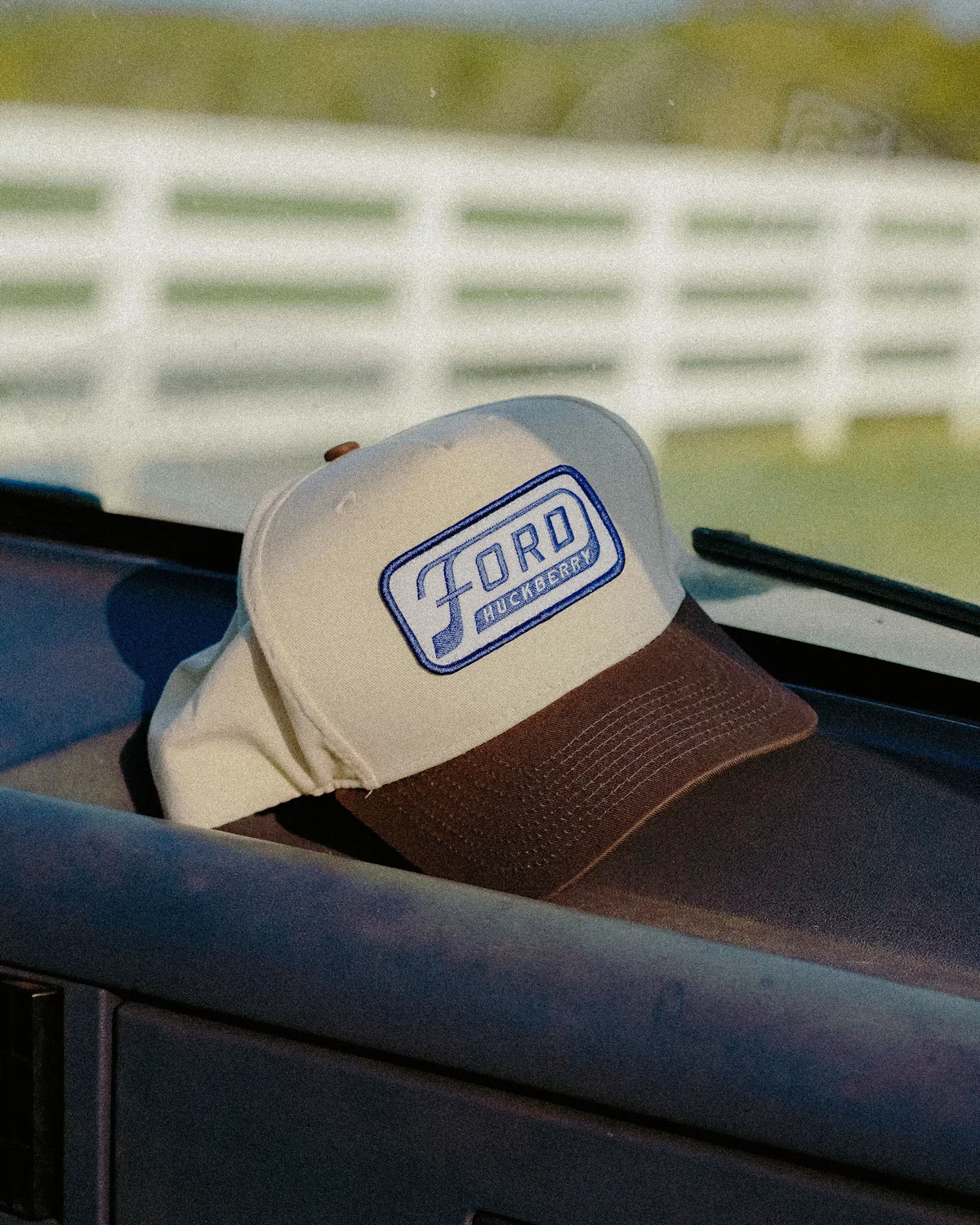 Cream and brown Ford × Huckberry cap resting on a truck dashboard