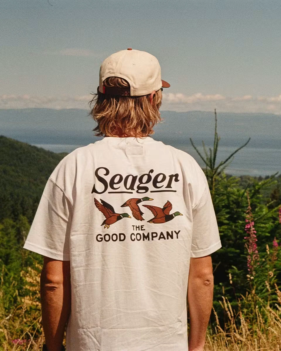 Seager Good Company graphic T-shirt viewed from the back against a mountain landscape