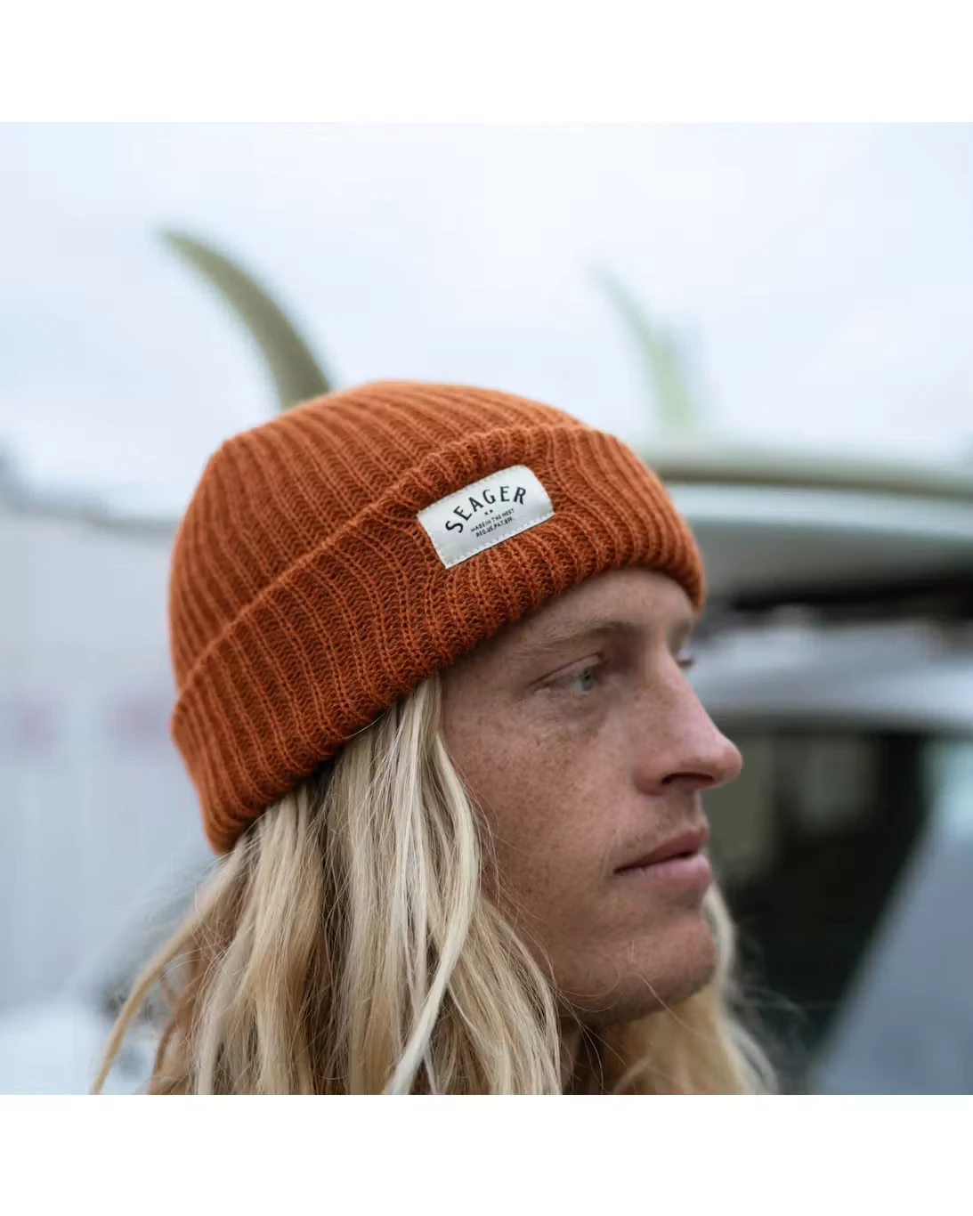 Rust Seager cuffed knit beanie with a cream woven label, worn outdoors