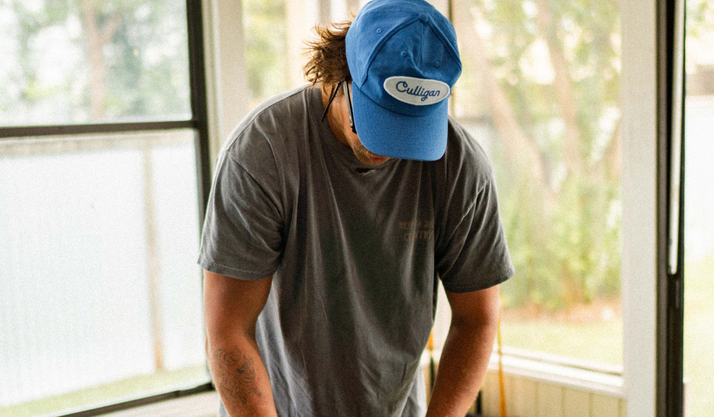 A finished blue Culligan cap worn in natural light beside sunlit windows